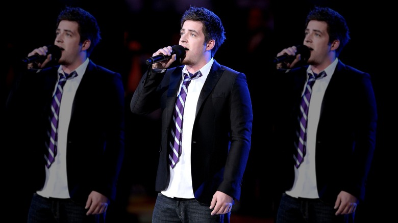 Lee DeWyze in a blazer and tie, singing into a microphone, lit blue