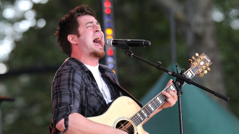 Lee DeWyze singing onstage with a guitar, his eyes closed and his mouth open wide