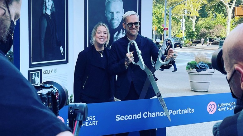 Bob Harper cutting a ribbon with a big pair of scissors outside his portrait exhibit