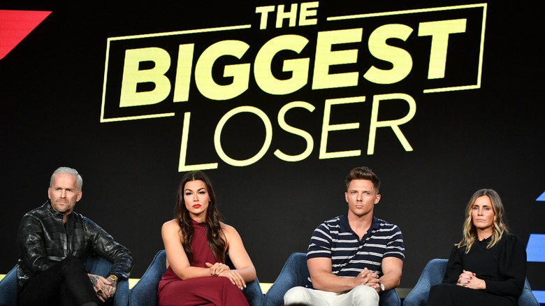 Bob Harper, Erica Lugo, Steve Cook, and Heather Olander sitting onstage under The Biggest Loser's new logo