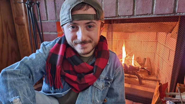 Atticus Shaffer smiling in front of a fireplace.