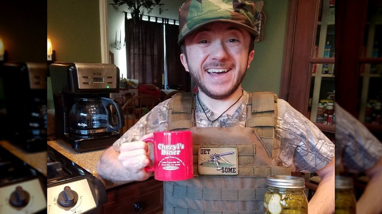 Atticus Shaffer smiling in the kitchen with coffee and pickles in hand.