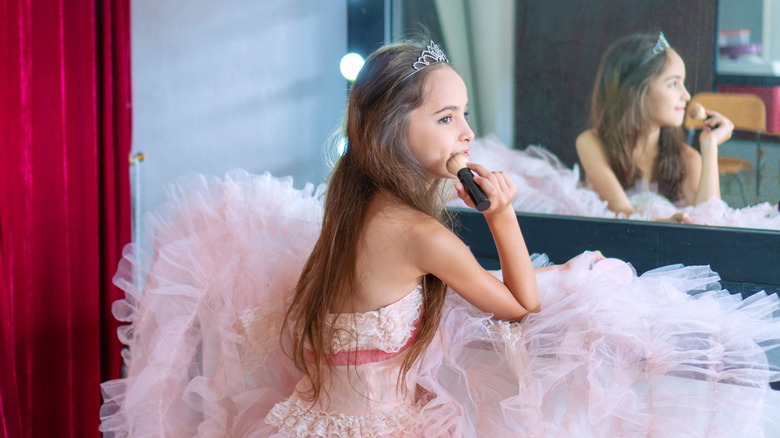 A young girl in a pink dress puts on makeup.