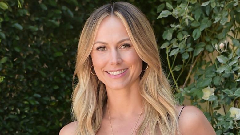 Stacy Keibler smiling in front of a hedge