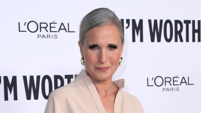 Andie MacDowell smirking in a white outfit while on the red carpet of the 19th annual L'oreal Paris Women of Worth celebreation event.