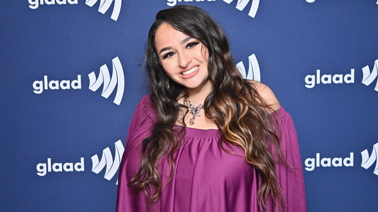 Jazz Jennings smiles at the glaad awards wearing a purple dress with her curly hair down.