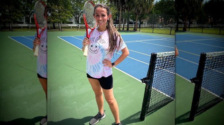 Jazz Jennings holds a racket on a tennis court smiling