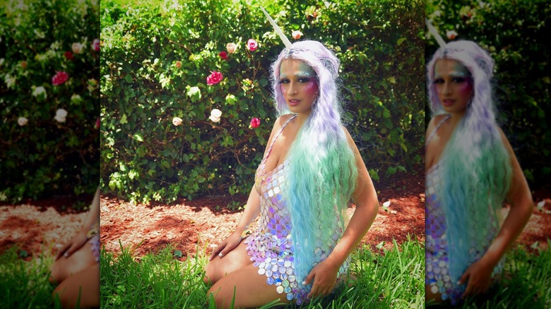 Jazz Jennings is dressed as a unicorn in a sequin dress and sits on the grass wearing a wig
