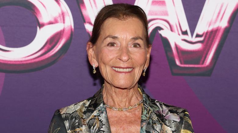 Judge Judy smiling in front of a purple backdrop