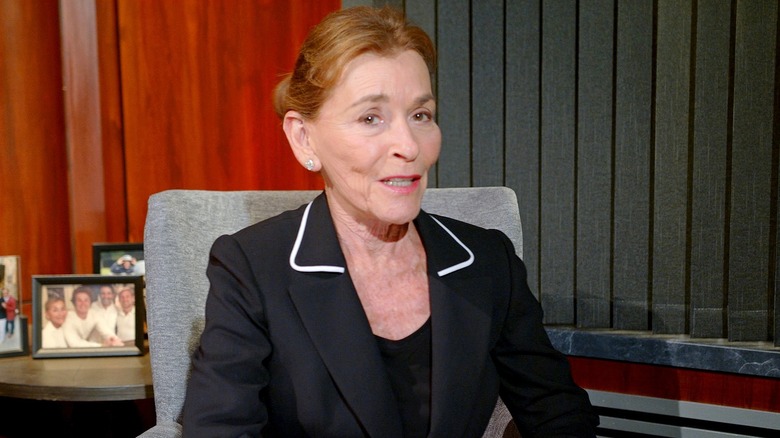Judge Judy in a smart black blazer, sitting in an office.