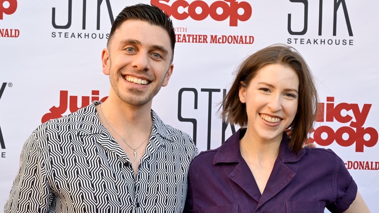 Brock Ciarlelli wearing a black and white patterned shirt and posing with Eden Sher, who is wearing a purple collared shirt