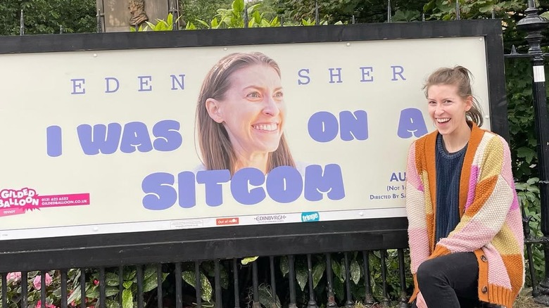 Eden Sher posing with an ad for her show "I Was on a Sitcom"
