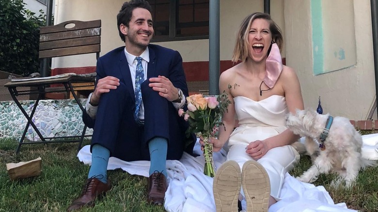 Eden Sher and her husband on their wedding day with their dog sitting on grass laughing