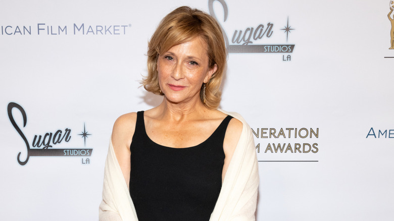 Actor Hallie Todd posing in a black dress and white sweater on the red carpet.