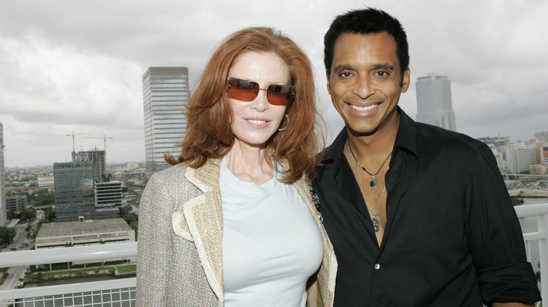 Mary Ann Pascal smiling in sunglasses posing outside next to a Vegas CEO in front of a cloudy skyline.