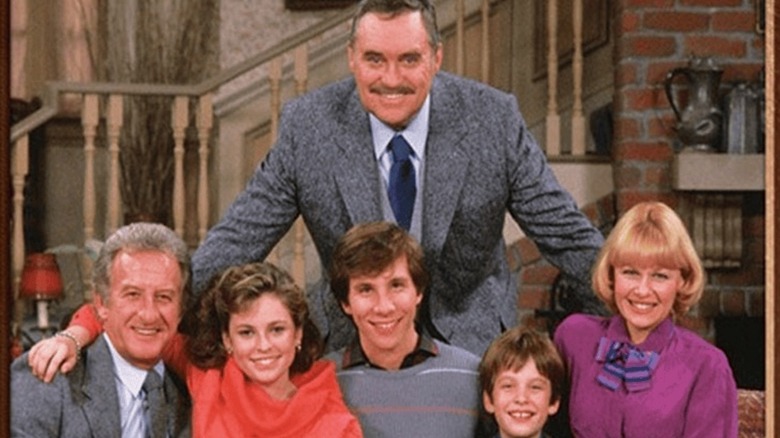 The cast of Mr. Belvedere smiling in the opening credits of the sitcom sitting on a couch with the butler standing behind them.