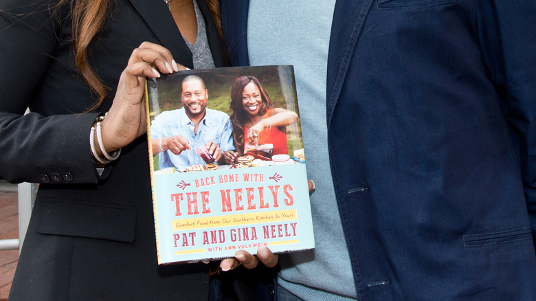 Hand of Gina Neely holding the book Back Home with the Neelys: Comfort Food from Our Southern Kitchen to Yours: A Cookbook