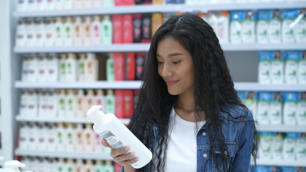 woman looks at bottle of shampoo at drugstore