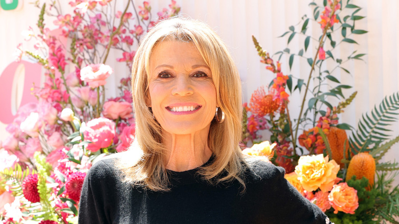 Vanna White smiles in front of floral bouquets in a black sweater