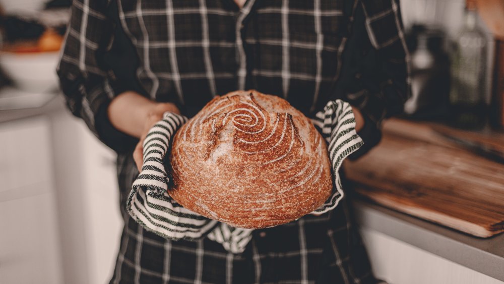 A woman holding a loaf of sourdough bread