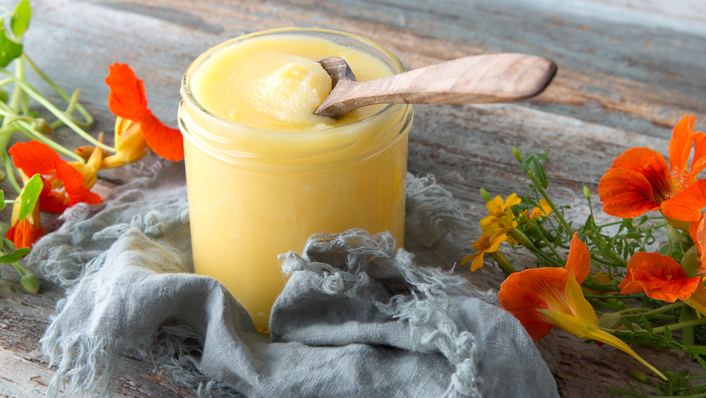 A glass jar filled with ghee, surrounded with flowers on a wooden table