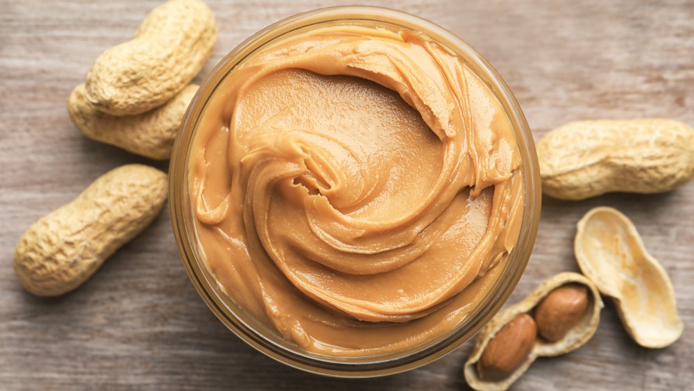 A jar of peanut butter and peanuts from above
