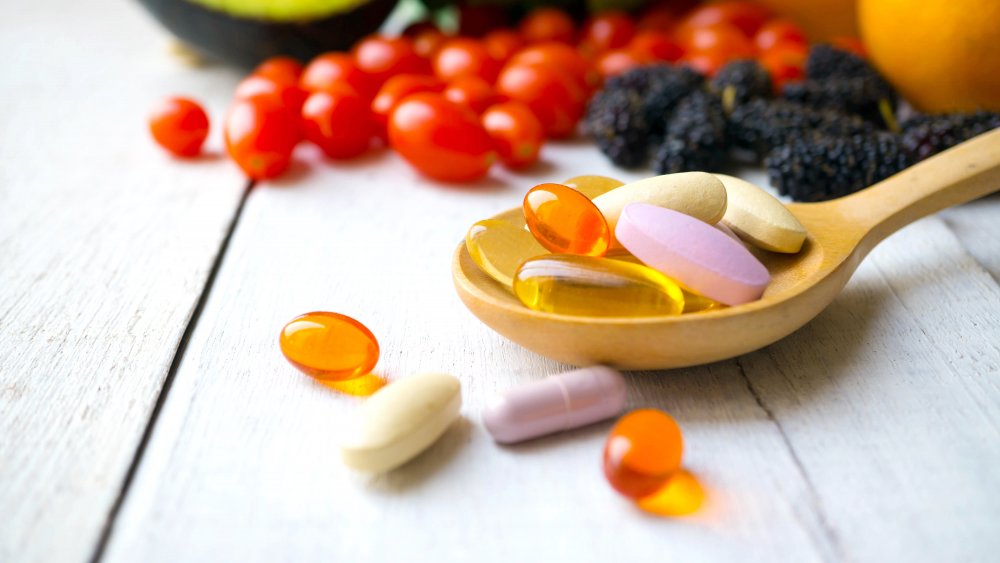 Pills in a wooden spoon with fruit in the background