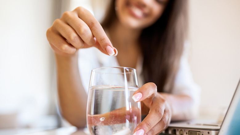 Woman putting antacid in glass of water