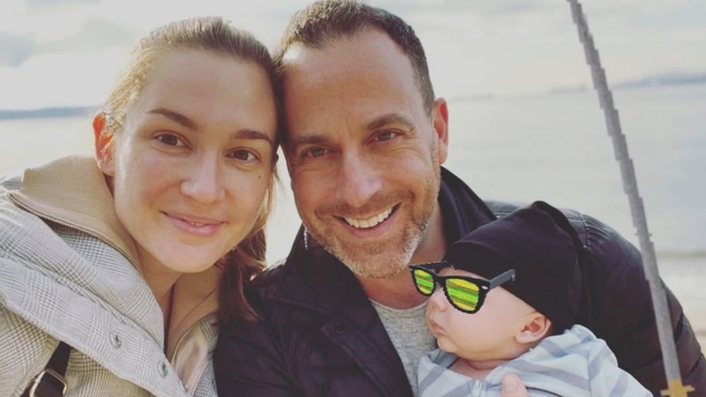 Katherine Barrell and Ray Galletti pose outdoors with their infant son.