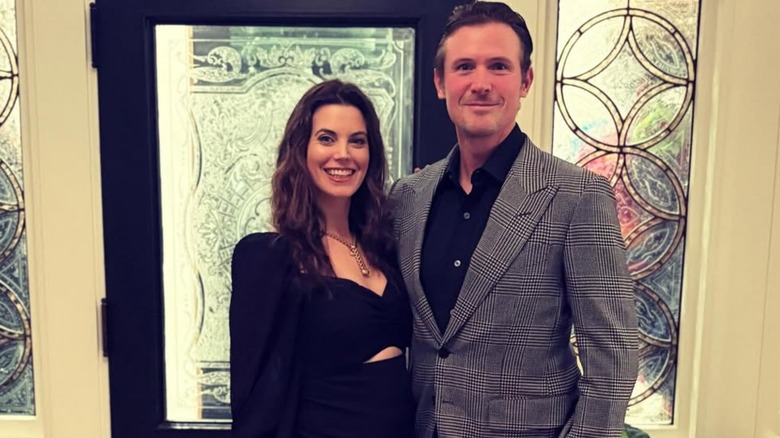 Meghan Ory and John Reardon pose in front of windows and a door.