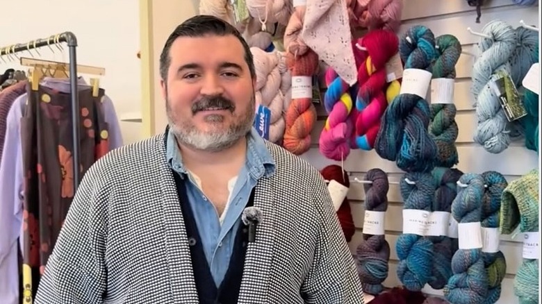 Sergio Guadarrama posing in front fo a wall of yarn