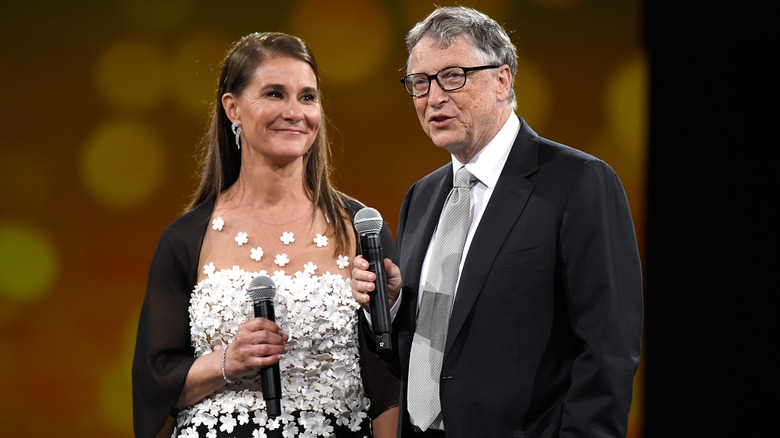 Melinda Gates smiling at Bill Gates while both hold microphones