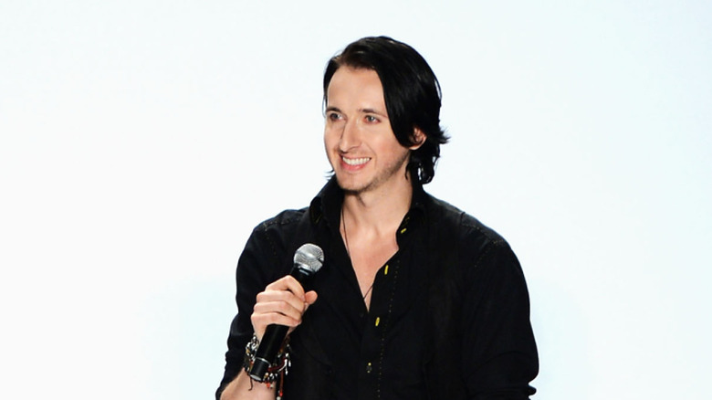 Dmitry Sholokhov speaking into a microphone onstage at 2013 Mercedes-Benz Fashion Week.