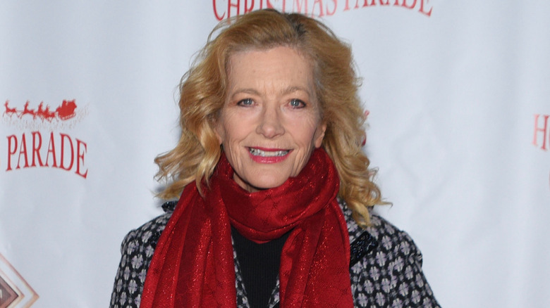 KiKi Ebsen smiles wearing a red scarf and black coat with her hair down on the red carpet at an event