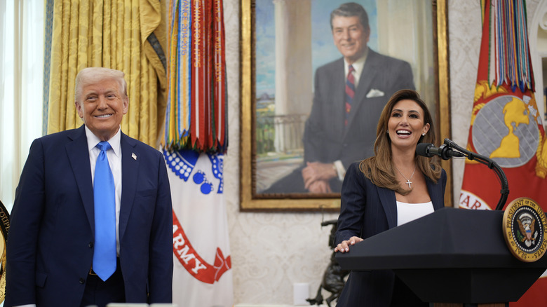 Donald Trump smiles as Alina Habba speaks at a lectern in the Oval Office.