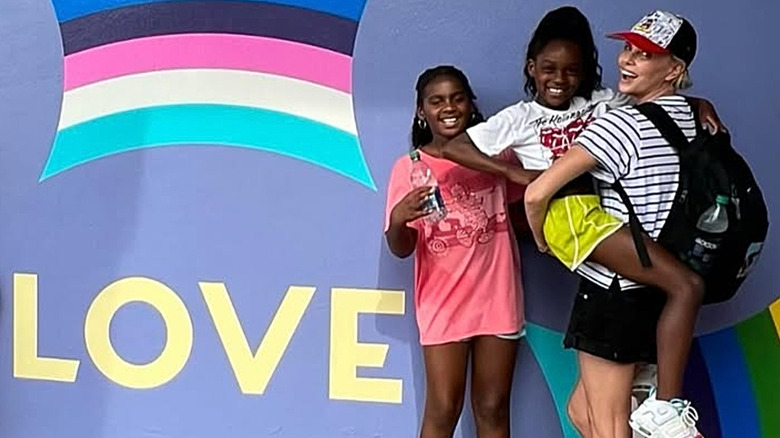 Charlize Theron and her daughters smiling at Disney World next to a Love sign