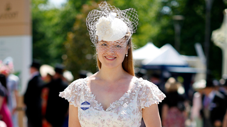 Flora Vesterberg smiles outside wearing a lace net headpiece and a v-neck white lace dress