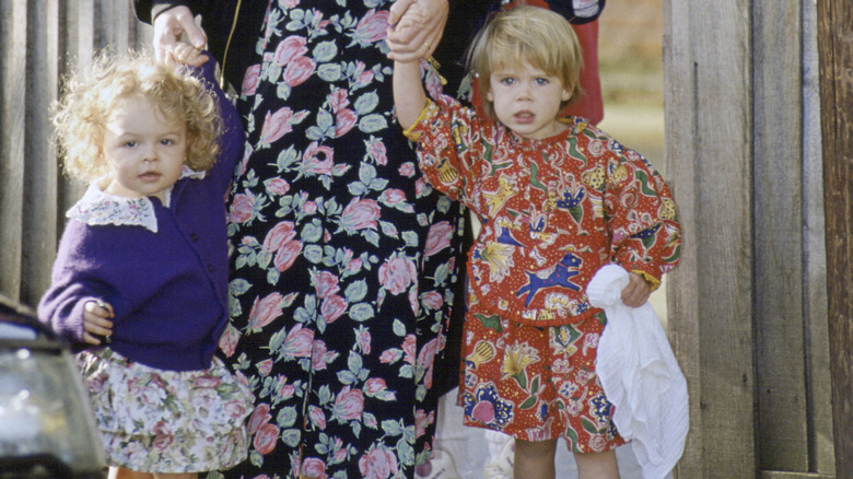 A young Zenouska Mowatt and Princess Eugenie holding an adult's hand outside