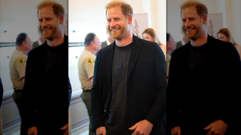 Prince Harry smiling in a black blazer and gray shirt