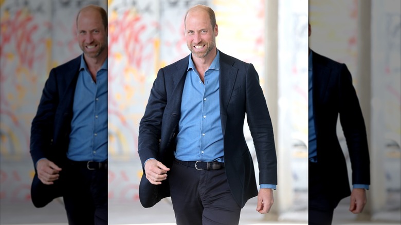 Prince William walking and smiling in a blue suit and open collar blue dress shirt