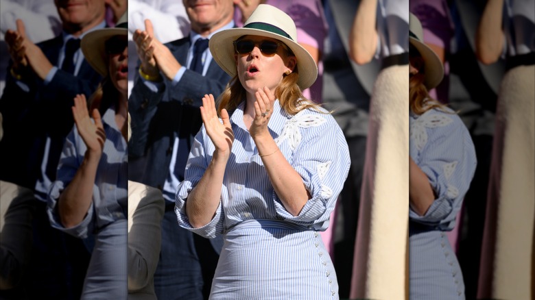 Princess Beatrice in blue and white outfit with hat and dark glasses clapping at Wimbledon