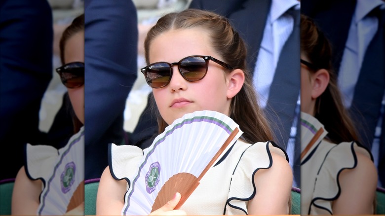 Princess Charlotte in white dress with black trim wearing sunglasses and holding a fan