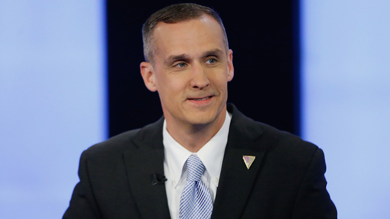Corey Lewandowski in a black suit and light blue tie smiling
