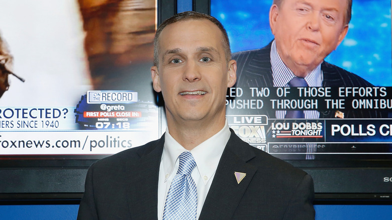 Corey Lewandowski smiling while standing in front of a TV screen