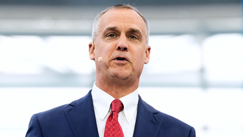 Closeup of Corey Lewandowski in a suit and red tie speaking while wearing a microphone headset