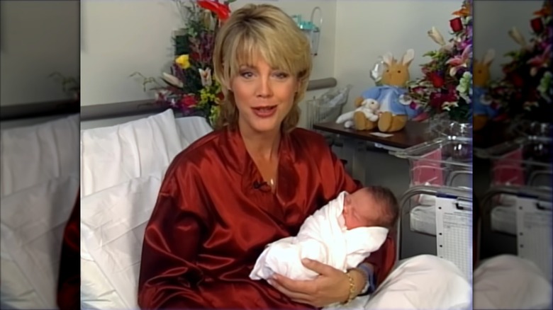 Deborah Norville anchoring from her hospital room while cradling her newborn baby