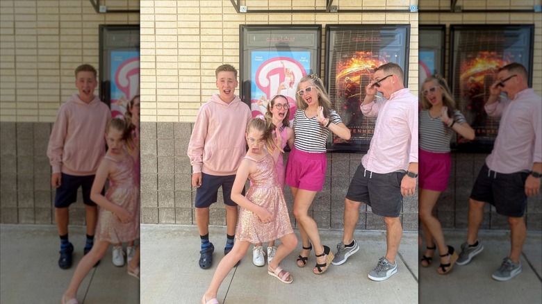 Kelly and Clint Harp strike silly poses with their kids in front of the Barbie movie poster