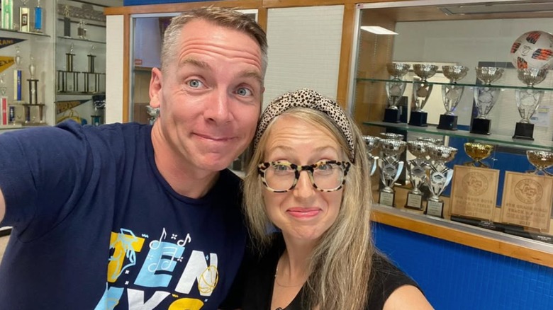 Clint Harp and Kelly Harp posing in front of a school trophy case