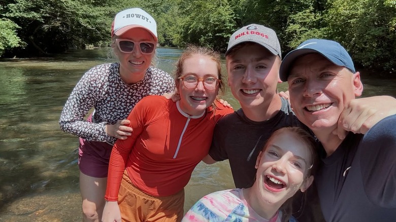 Clint and Kelly Harp smile in a creek outside with their three children