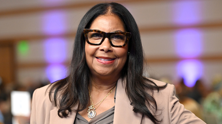 Cookie Johnson smiling in glasses and tan jacket